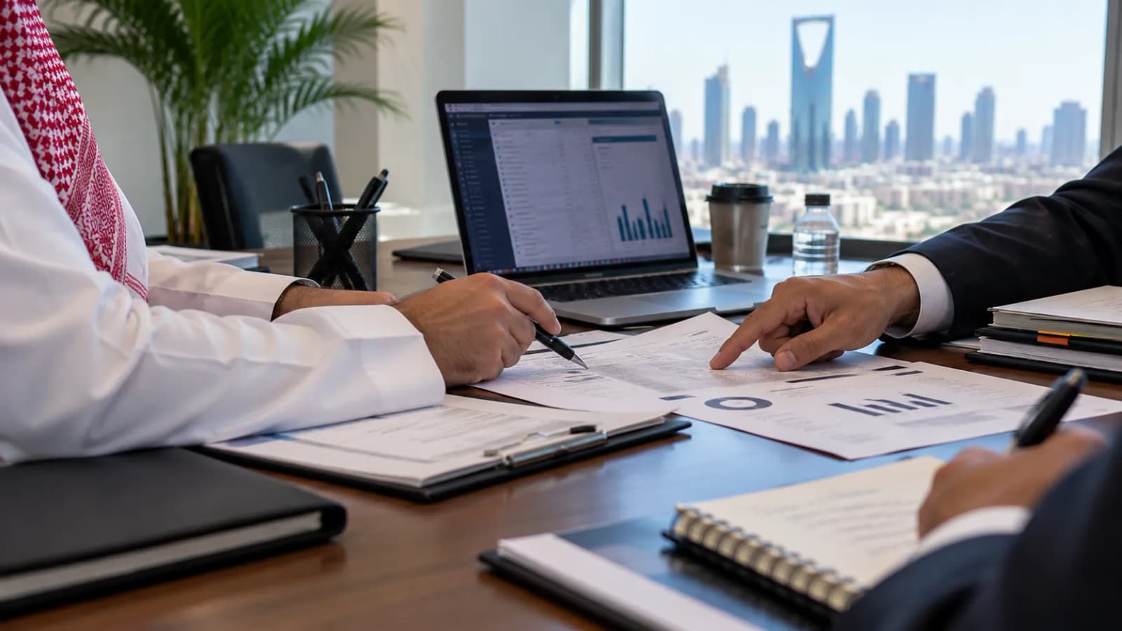 Two people going through a findings report at a meeting table, charts and a laptop between them.
